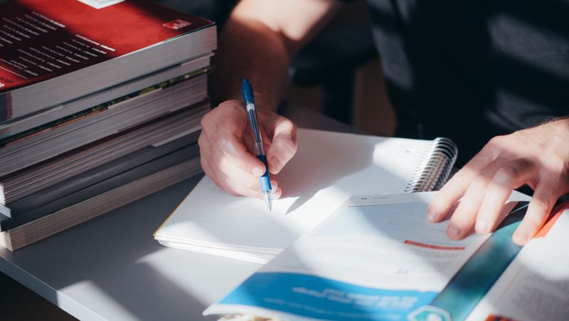 A person writing study notes in a notebook next to textbooks.