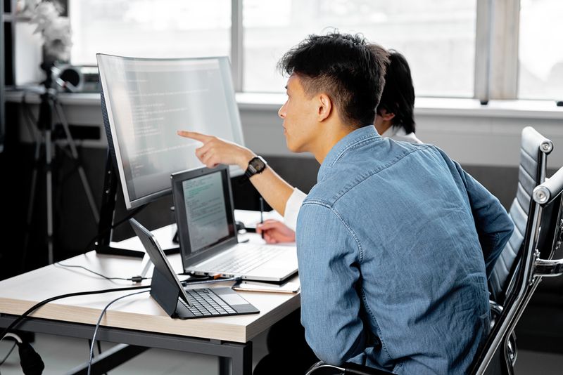 People collaborating at a tech workspace with laptops and monitors.